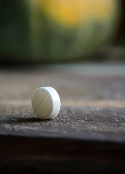 A round tablet stands ribbed on the table.Tablet close-up on a wooden table. white pill - traditional medicine.