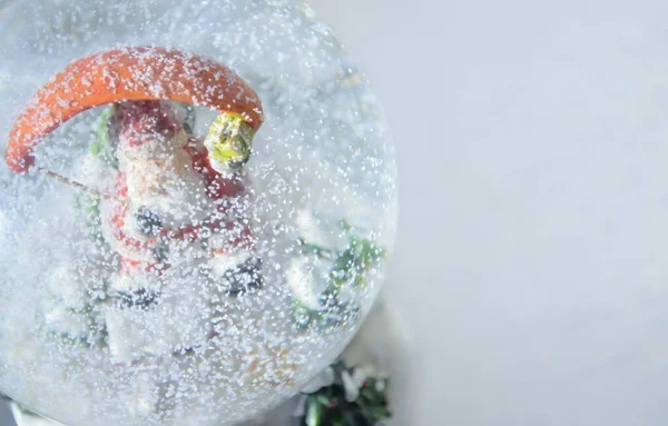 In the snow globe is Santa Claus. The focus is blurred because of the snow. Snow falls in the globe. A snow toy.