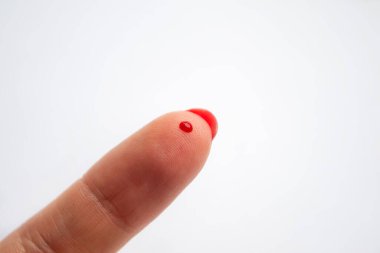 İşaret parmağında bir damla kan. Beyaz arka plan. Parmaklarda bir damla kan. Deride kırmızı bir kan damlası.