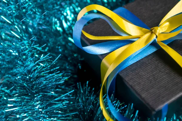 In blue tinsel is a gift with a yellow-blue ribbon. The black gift is tied with a yellow-blue ribbon. Christmas and New Year - a gift of the symbol of Ukraine.