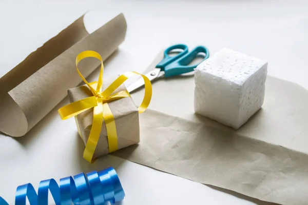 Wrapping gifts with yellow-blue ribbon. On a white background, styrofoam packaging paper, scissors and tape. Christmas and New Year - gift wrapping.