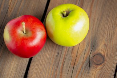 Tahtanın üzerinde bir kırmızı ve bir yeşil elma yatar. Ahşap bir masada kırmızı ve yeşil elma. Sağlıklı meyveler masada..