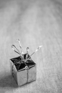 Gri tonlu bir minimalizm hediyesi. Masada bir hediye var. Parlak bir paketin içinde hediye olan kutu bir kurdeleyle bağlanmış. Masaya bir hediye..