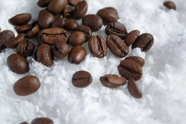 Coffee beans in the snow. Coffee beans are scattered on the white snow. Coffee contrasts with white snow.