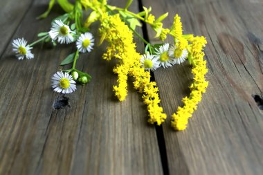 Wildflowers on a wooden table. There are several meadow flowers on the board. Yellow flowers with daisies on the table.