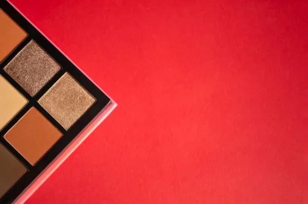 a palette of shadows on a red background. Palette with fashionable shadows of brown shades. Fashionable eyeshadow on the red table.