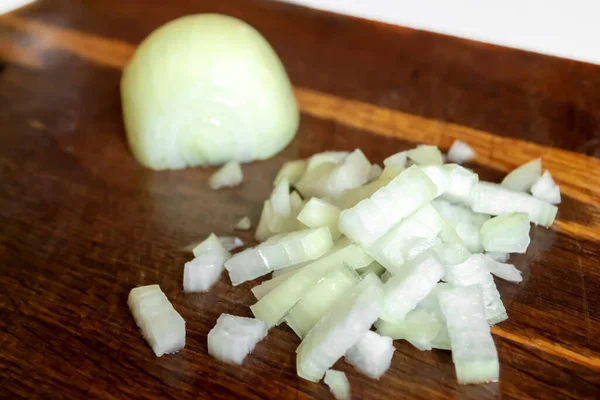 On a wooden board, half an onion and a second, chopped half. Chopped onions on a wooden board. Chopped onions on the table.