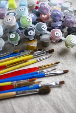 Fırçalar renkli boyaların yanında yatar. Çarşaf kumaşında fırçayla çizim yapmak için resimler. Çizim için renkli fırçalar ve boyalar.