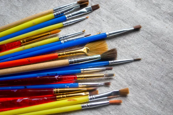 Lots of colored brushes for drawing. Brushes for artists on linen fabric. There are many artistic tassels on the fabric.