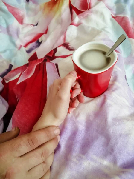 Coffee in bed, hand of a man and a woman. A man holds a woman\'s hand with coffee.