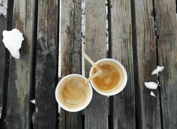 Two cups of coffee on wooden boards. Paper cups with wooden sticks and frothy coffee. Top view of the coffee cups outside.