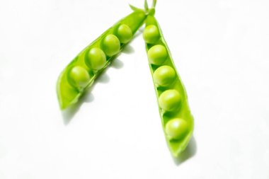 Green peas on the table. On a white background is an open pod of green peas. Green pea pods with young beans.