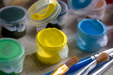 Paints on the table next to the brushes. Watercolor paints for drawing and brushes. Yellow and blue paints on the table in jars.