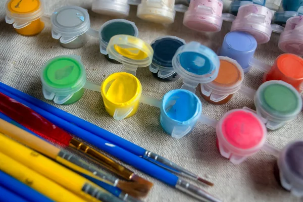 Paints on the table next to the brushes. Yellow and blue paints on the table in jars. Watercolor paints for drawing and brushes.