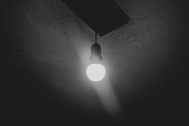 A light bulb is on in a dark basement. One light bulb on the ceiling. The ominous atmosphere is a light bulb in a dark room.