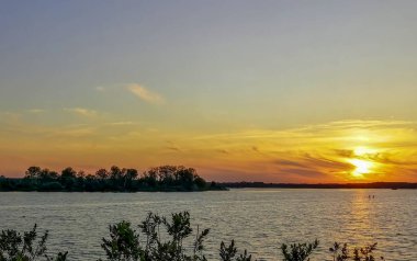 sunset on the water. On the shore of the lake there is a beautiful sunset. The sun magically sets over the horizon.