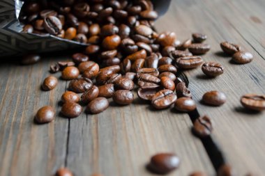 Coffee beans are scattered around the table. Fresh coffee beans from a pack. Arabica coffee beans poured out of the bag onto a wooden table.