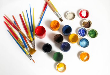 For artists, there are a lot of colored paints and brushes. Watercolor paints next to the brushes. Paints and brushes on a white background. Oil paints on the table.