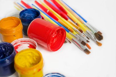 watercolor and oil paints on a white table. Jars of colored paint stand next to the brushes. For artists, there are a lot of paints and brushes.