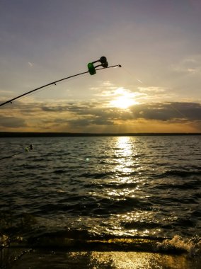 Fishing at sunset. Fishing rods in the light of the setting sun. Evening fishing. One fishing rod against the backdrop of the setting sun.