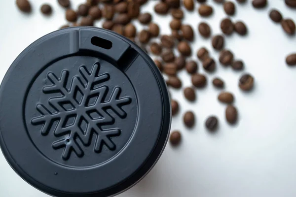 A cup of paper with a fish on a white background among the grains of the horse. Plastic cover about a snowflake on a coffee cup. winter cup among coffee beans.