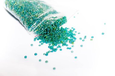 Green beads on a white background. Small beads on a white background for weaving. Material for handmade - weaving with a bisser - a lot of green beads.