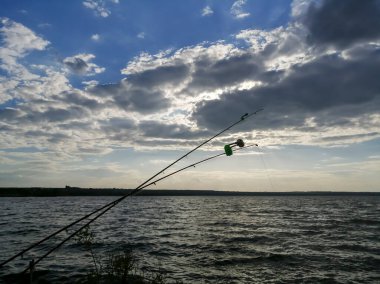 Fishing rods in front of a beautiful horizon. A bluebell for fishing rods on the background of the horizon. Roar - the sun sets. Fishing at sunset.