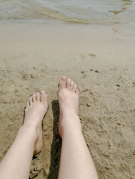 A girl\'s feet on the beach. On the sand are the girl\'s feet. The feet of a white woman on the soft sand on the beach. Beautiful legs.