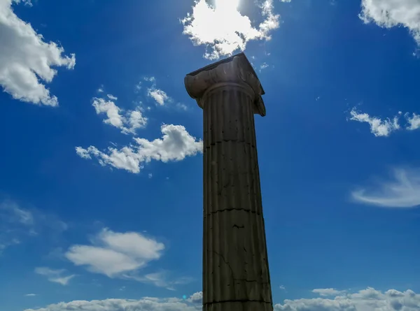 A dark column covers the sun. An antique column against a cloudy sky. A column opposite the sun in the shade. Roman collonna.