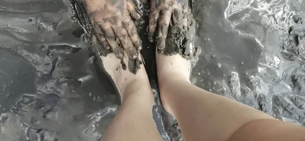 Mud baths for feet. The girl\'s feet are covered with healing mud. Hands smear the feet with therapeutic mud. Useful beauty treatments for health and beauty.