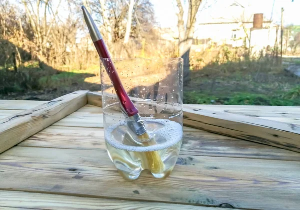 construction brush in a glass with paint solvent. The used brush is cleaned in a transparent jar with solvent. A brush in the water.