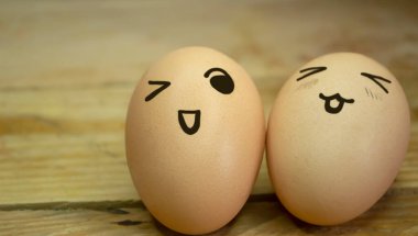 Ahşap bir tahtanın arka planında iki tane emoticonlu yumurta. Tahta bir masanın üzerinde emojili iki yumurta var. Yumurtalarda, çizimler duygulardır. Bir gülücük ve yumurtalara göz kırpma.