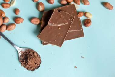 Ev yapımı çikolata için malzemeler. Mavi arka planda bir çikolata kalıbı var. Fıstık ve kakao tozlu shozhka..