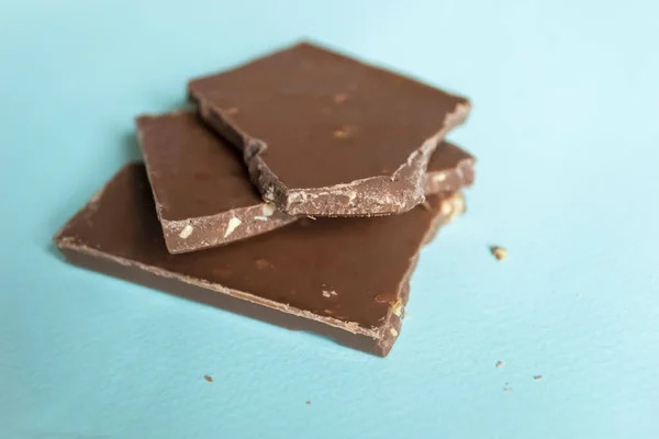 Pieces of broken chocolate on a blue background. A broken chocolate bar is insulated. Delicious dessert chocolate.
