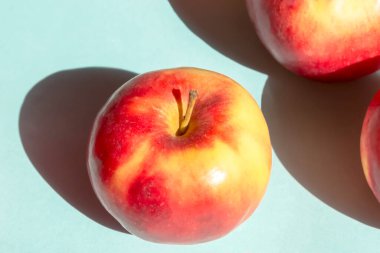 Mavi arka planda güzel kırmızı elmalar. Güneş ışığının parlak gölgesi. Güneş ışığı elmaların üzerine düşer ve sert bir gölge yaratır. Faydalı meyveler - elma.