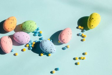 Mavi arka planda Paski yumurtaları ve renkli tozlar uzanıyor. Renkli paskalya yumurtalarının yanında sarı ve mavi boncuklar..