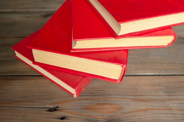 Books with a red cover on a wooden table. Textbooks for school and college. On a wooden background lies several books with a red cover.