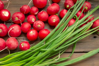 Turp, ahşap bir masada yeşil soğanların yanında yatar. Salata için bahar sebzeleri. Baharın başında kullanışlı ürünler. Baharda mevsimlik sebzeler.