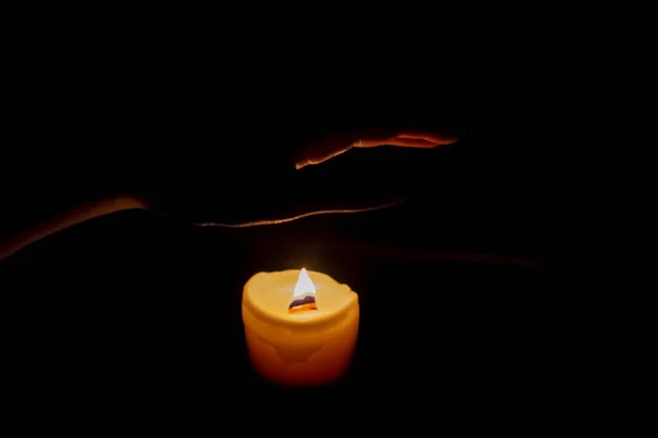 在黑暗中 一只手伸出手去拿一支燃烧的蜡烛 烛光昏暗地照在手上 手和蜡烛在黑暗的房间里 蜡烛的温暖温暖了皮肤 — 图库照片