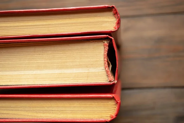 The spines of books with a red cover. Three books stand side by side on a wooden table. The end of the book is dense sheets of a closed book.