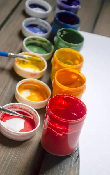 Colored paints in jars on a wooden table. Flowers of the LGBT community or rainbow on the table. Paints for drawing different colors.