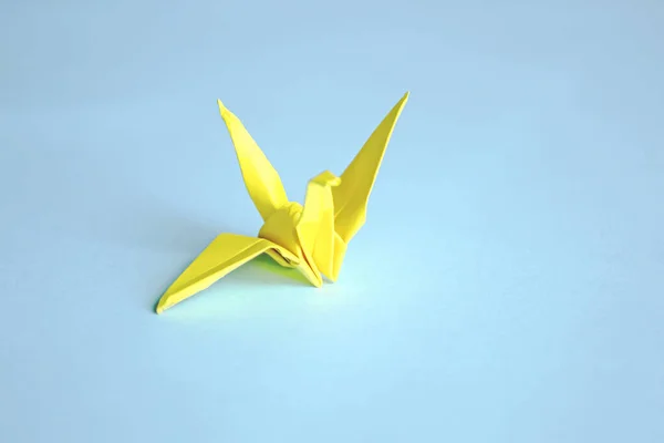 Yellow paper crane on a blue background. On a blue background there is one paper crane. Origami, Japanese culture is a crane.