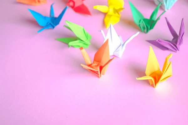 A lot of paper cranes on a pink background. Japanese origami culture - paper cranes. Fulfillment of desires - paper cranes made of colored paper.