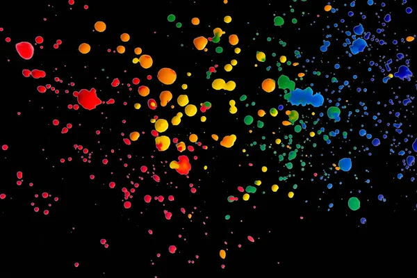 Colored spots of paint on a black background. There are many drops of colored paint on black paper. Splashes of paint on a black background.