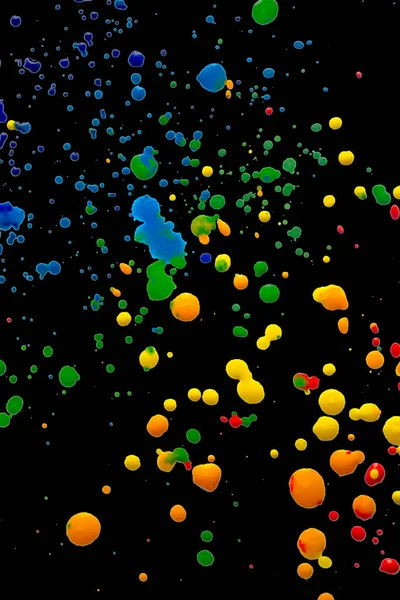 Colored spots of paint on a black background. There are many drops of colored paint on black paper. Splashes of paint on a black background.