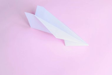 Pembe arka planda beyaz kağıt uçak. Pembenin üzerinde beyaz bir kağıt uçak yatıyor..