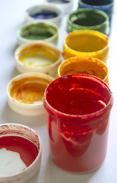 Colored acrylic paints in jars are in a row. Vertical photo of paint in jars. Jars of colored paint without lids.