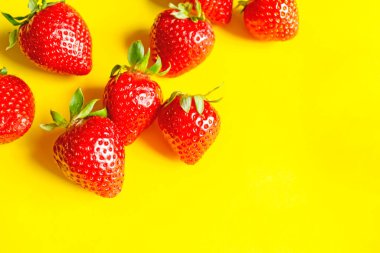 Sarı arka planda çilek yaprakları. Jetteki çileklerin parlak fotoğrafı. Sarı üzerine yaz meyvesi. Tatlı çilekler .