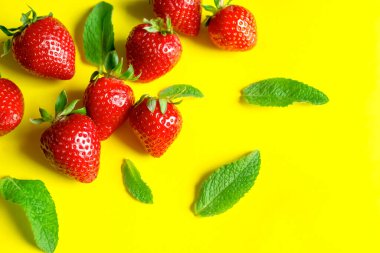Sarı arka planda nane aromalı çilekler. Kırmızı çilek ve yeşil naneli, güneşli bir arka plan. Yaz tazeleyici yemekler için malzemeler.