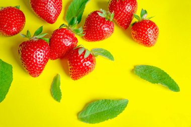 Sarı arka planda nane aromalı çilekler. Kırmızı çilek ve yeşil naneli, güneşli bir arka plan. Yaz tazeleyici yemekler için malzemeler.